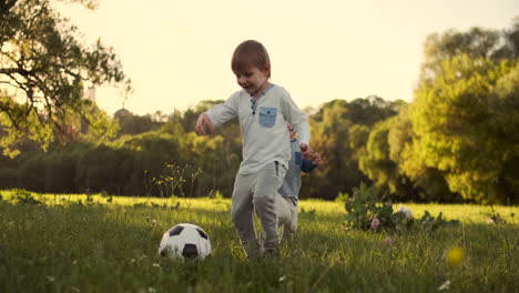 In-slow-motion-a-happy-boy-with-a-soccer-ball-runs-into-the-field-at-sunset-dreaming-of-playing-professional-football.
